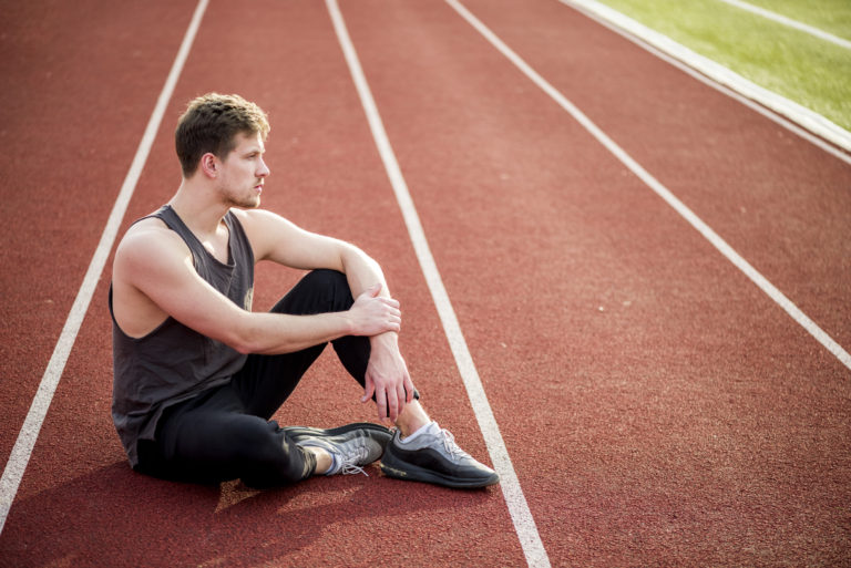 contemplated young male athlete sitting race track